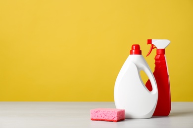 Photo of Bottles of cleaning products and sponge on light table. Space for text