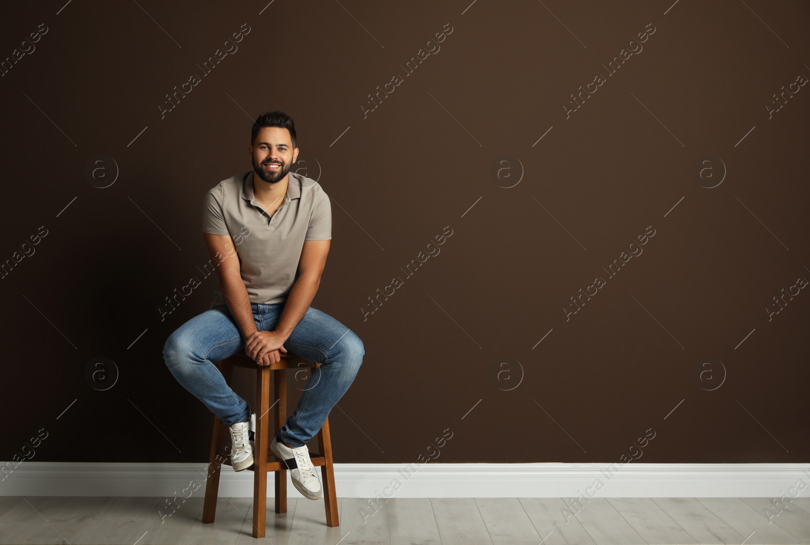 Photo of Handsome young man sitting on stool near brown wall. Space for text