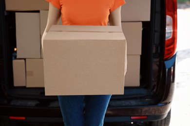 Courier holding package near delivery truck outdoors, closeup