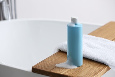 Photo of Bottle of bubble bath with foam and towel on tub in bathroom, space for text