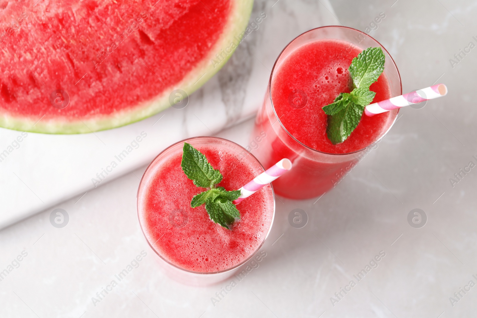 Photo of Tasty summer watermelon drink in glasses and board with sliced fruit on table, top view