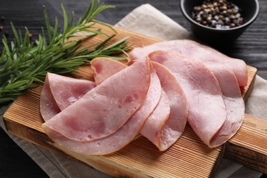 Photo of Slices of delicious ham with rosemary on dark wooden table, closeup