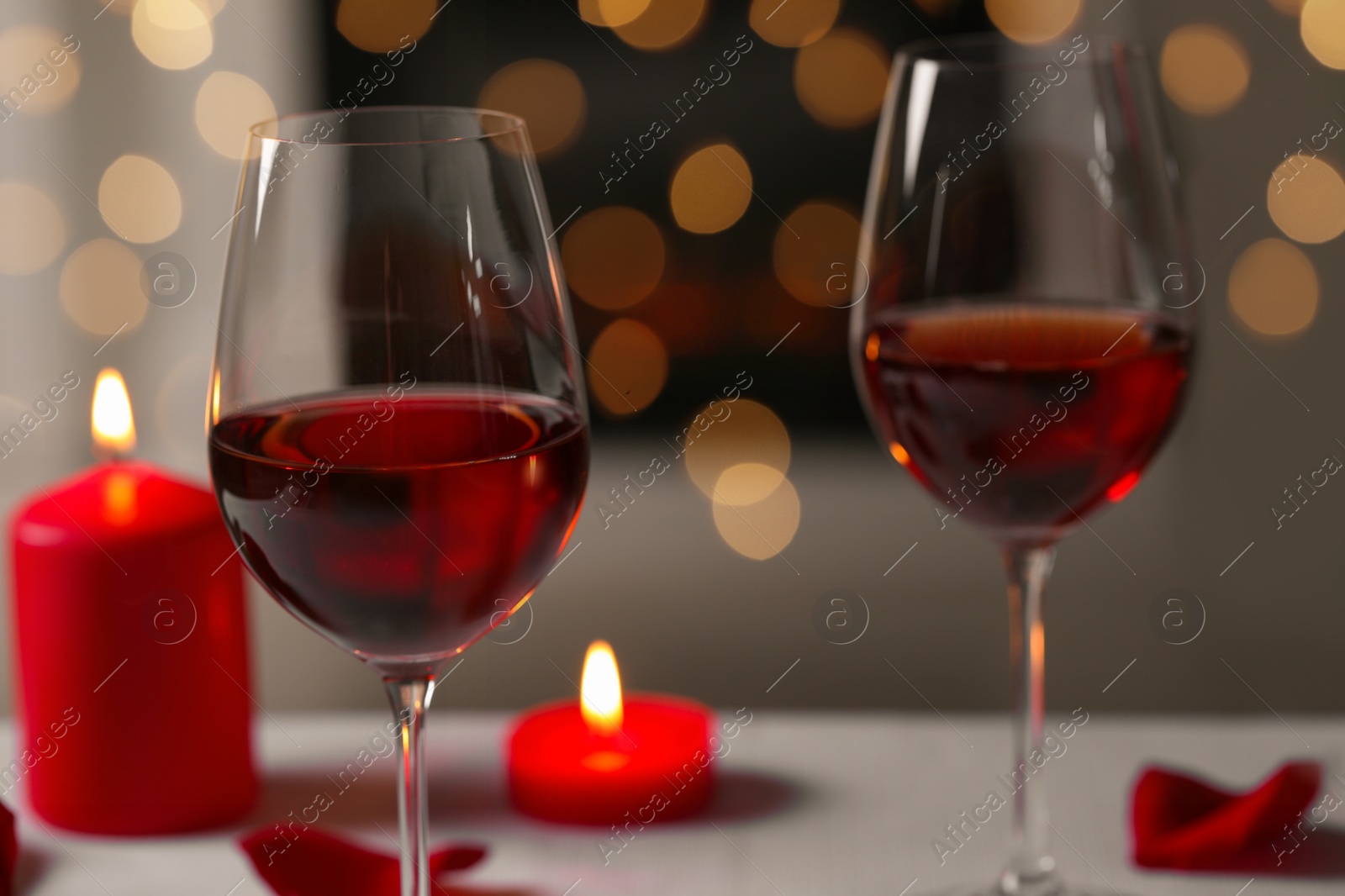 Photo of Glasses of red wine and burning candles against blurred background, space for text. Romantic atmosphere