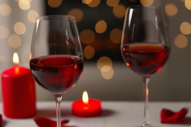 Photo of Glasses of red wine and burning candles against blurred background, space for text. Romantic atmosphere