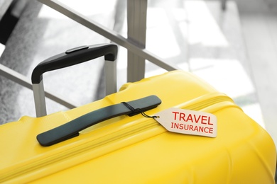 Photo of Yellow suitcase with TRAVEL INSURANCE label at stairs indoors, closeup