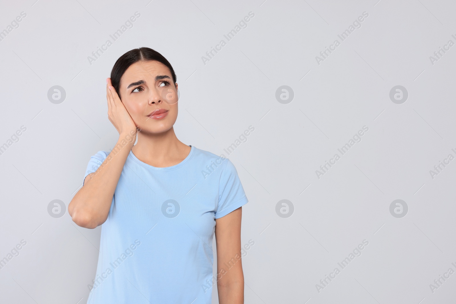 Photo of Young woman suffering from ear pain on light grey background. Space for text