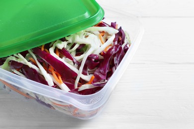 Fresh cabbage salad with shredded carrot in plastic container on white wooden table, space for text