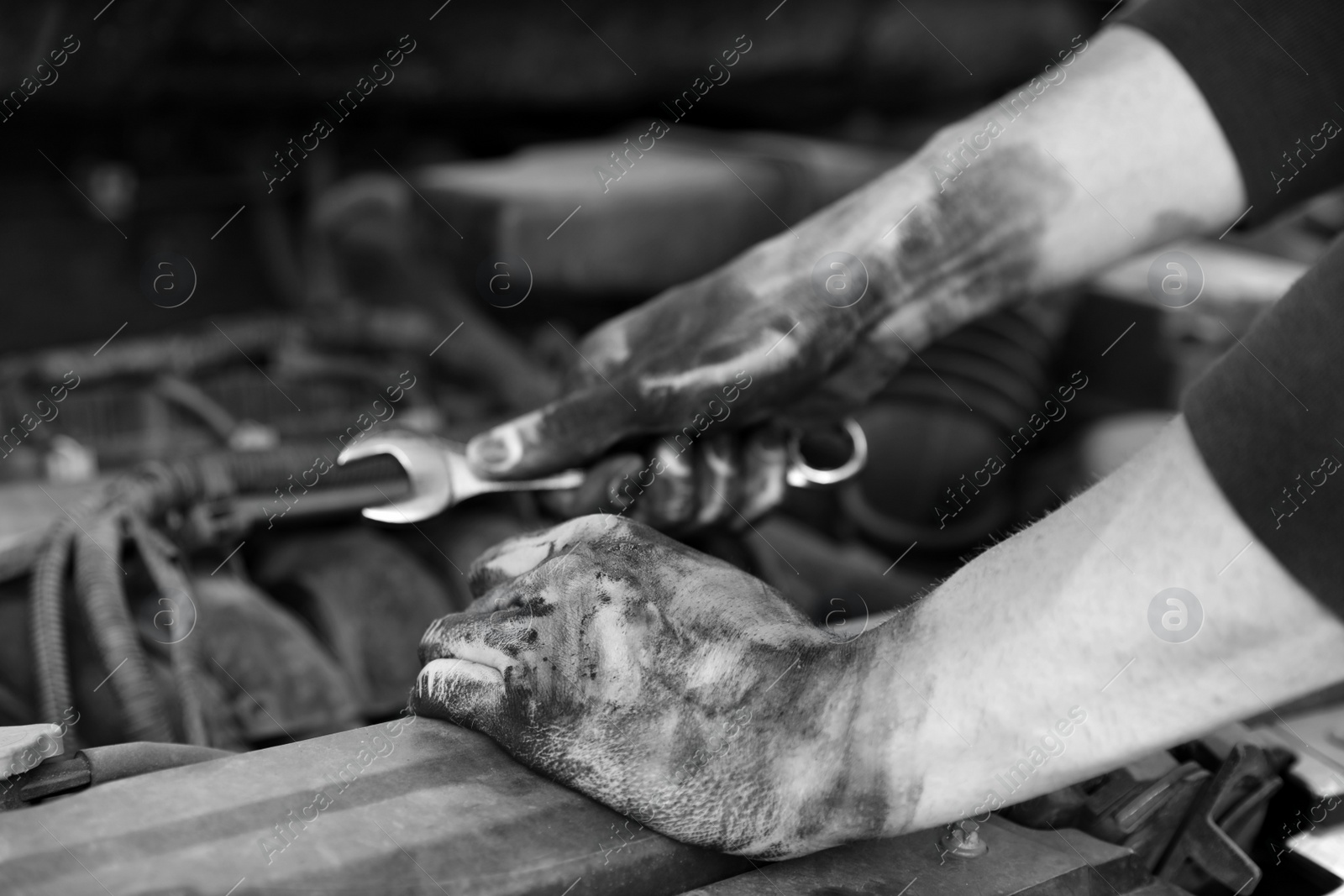 Photo of Dirty mechanic fixing car, closeup of hands. Black and white effect