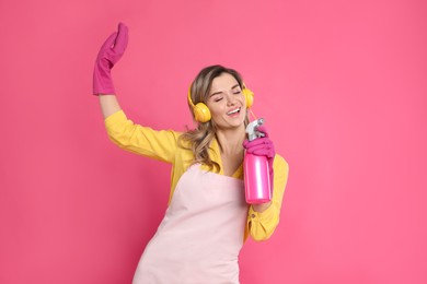 Photo of Beautiful young woman with headphones and bottle of detergent singing on pink background
