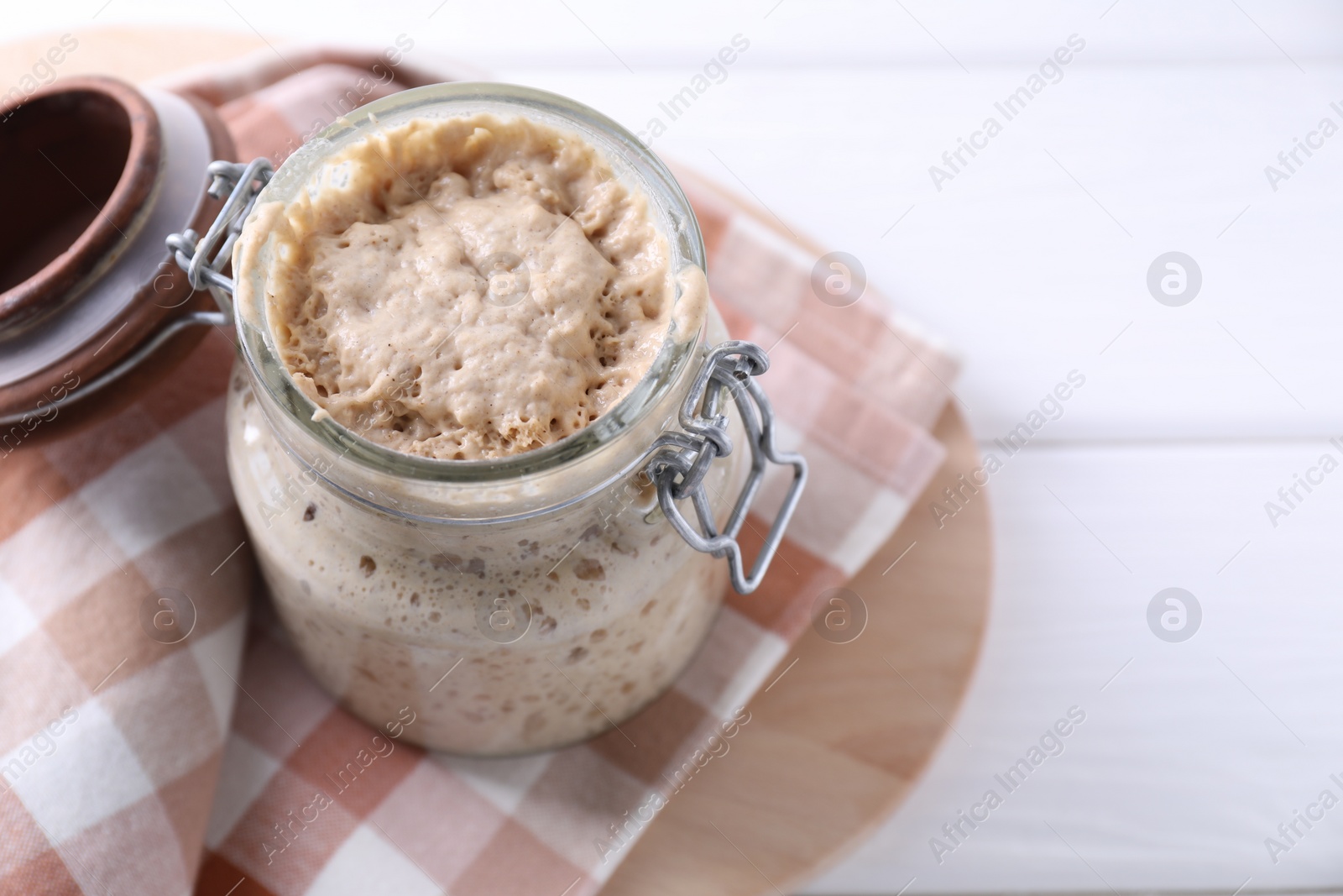 Photo of Sourdough starter in glass jar on white wooden table, closeup. Space for text