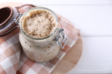 Photo of Sourdough starter in glass jar on white wooden table, closeup. Space for text