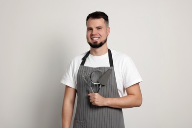 Happy confectioner in apron holding professional tools on light grey background