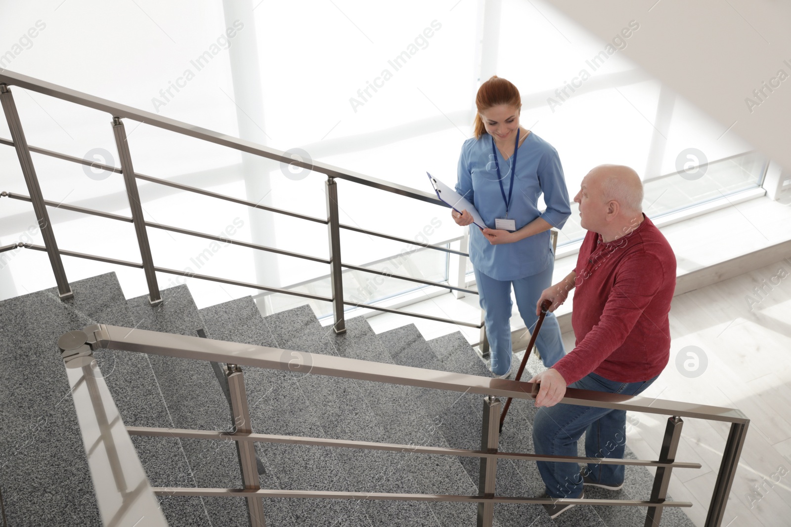 Photo of Nurse assisting senior man with cane to go up stairs indoors