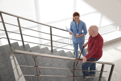 Photo of Nurse assisting senior man with cane to go up stairs indoors