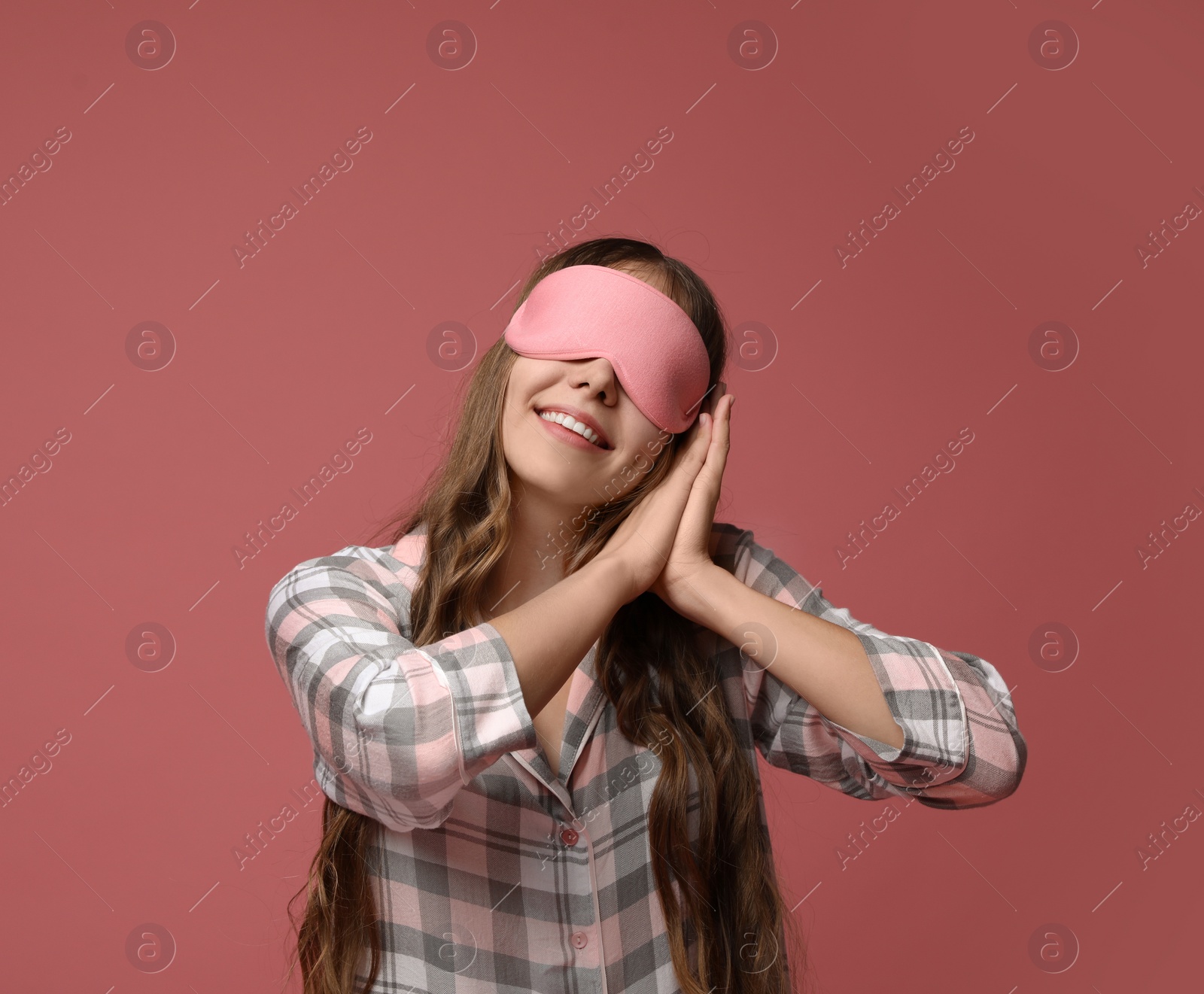 Photo of Young woman wearing pajamas and sleeping mask on dusty rose background. Bedtime