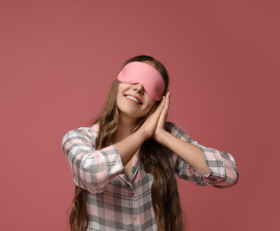 Young woman wearing pajamas and sleeping mask on dusty rose background. Bedtime