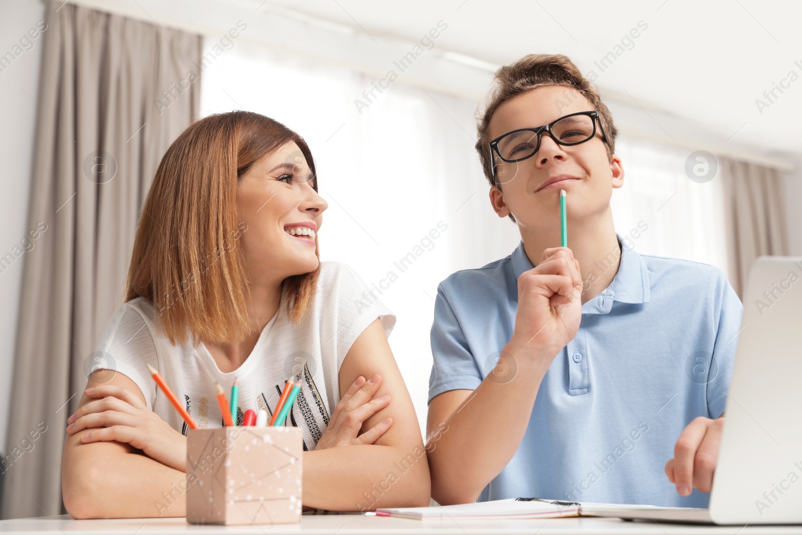 Photo of Mother helping her teenager son with homework indoors