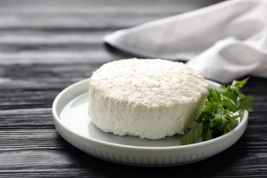 Photo of Delicious fresh cottage cheese with parsley on black wooden table, closeup