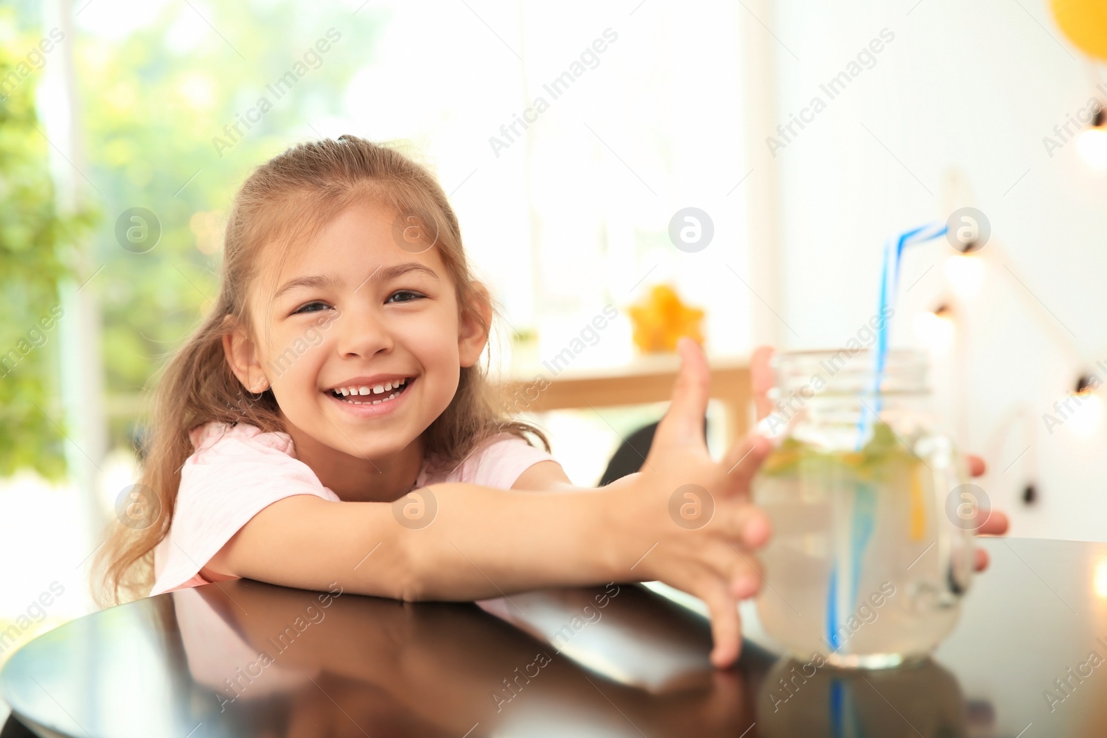 Photo of Little girl with natural lemonade at table indoors