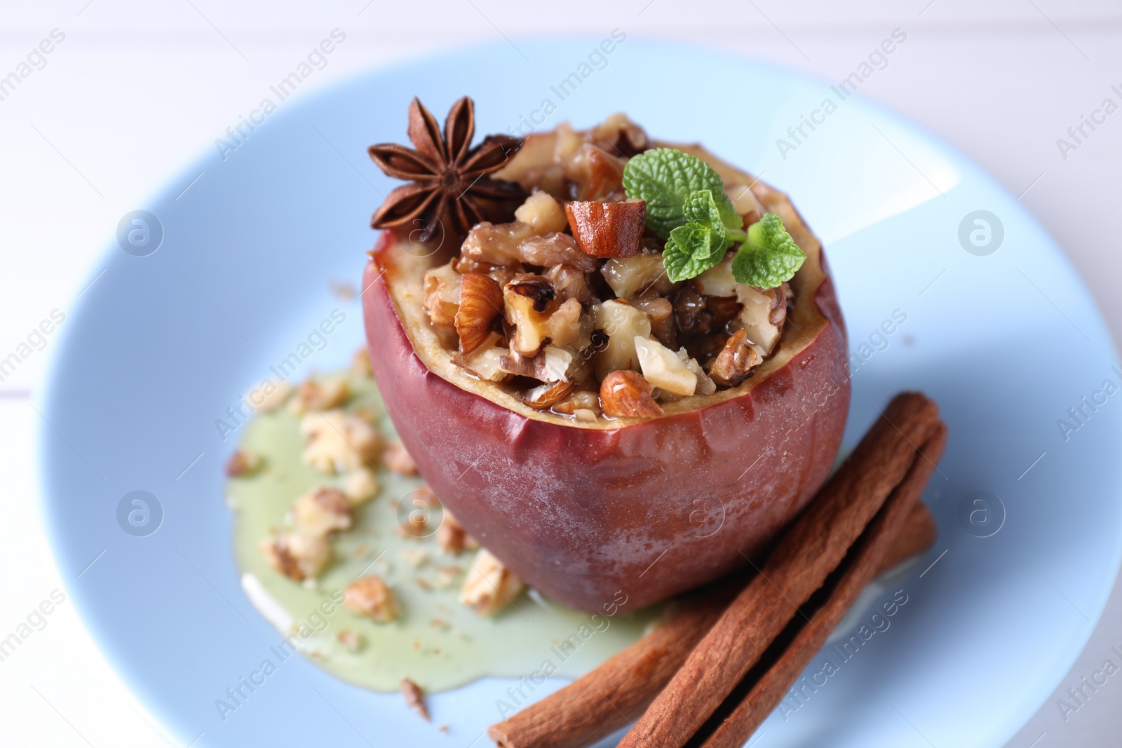 Photo of Tasty baked apple with nuts, honey, spices and mint on white table, closeup