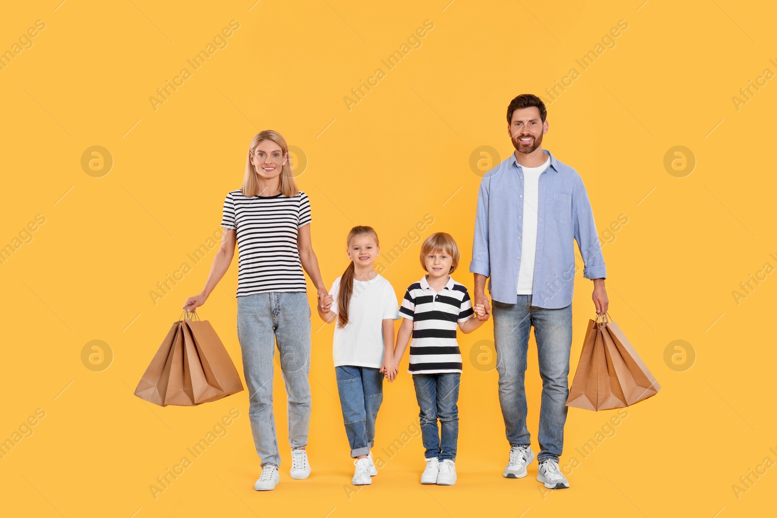 Photo of Family shopping. Happy parents and children with paper bags on orange background