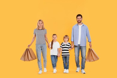 Photo of Family shopping. Happy parents and children with paper bags on orange background