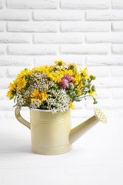 Beautiful bouquet of bright wildflowers in watering can on white wooden table near brick wall