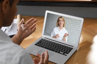 Image of Man talking with beautiful woman using video chat on laptop at wooden table, closeup. Online dating