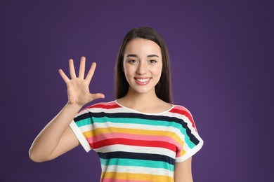 Photo of Woman showing number five with her hand on purple background