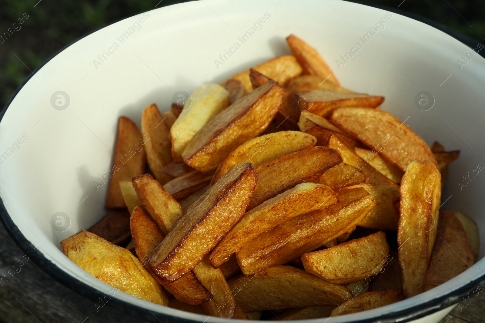 Photo of Metal bowl with delicious fried potato wedges on table, closeup