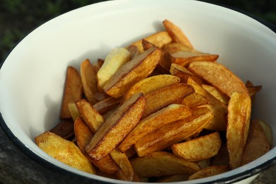 Metal bowl with delicious fried potato wedges on table, closeup