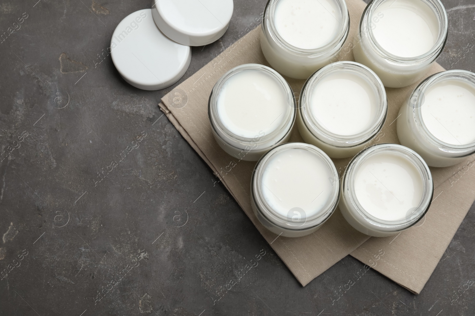 Photo of Tasty yogurt in glass jars on grey table, flat lay. Space for text