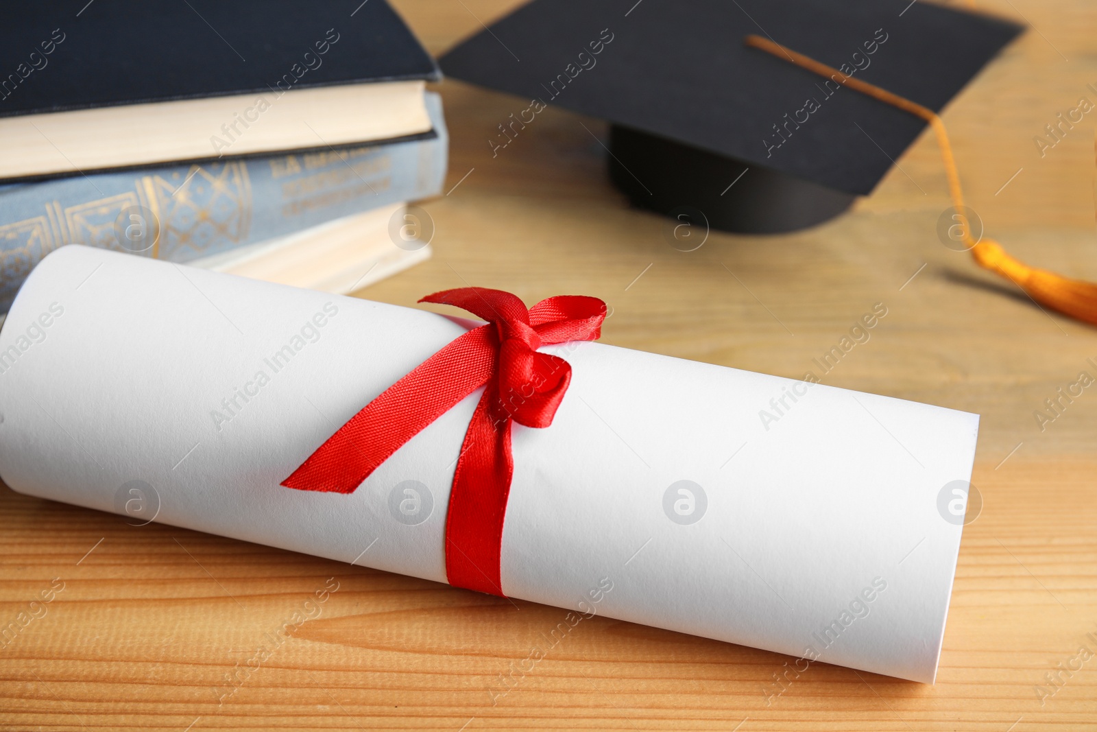 Photo of Graduation hat, books and student's diploma on wooden table, closeup