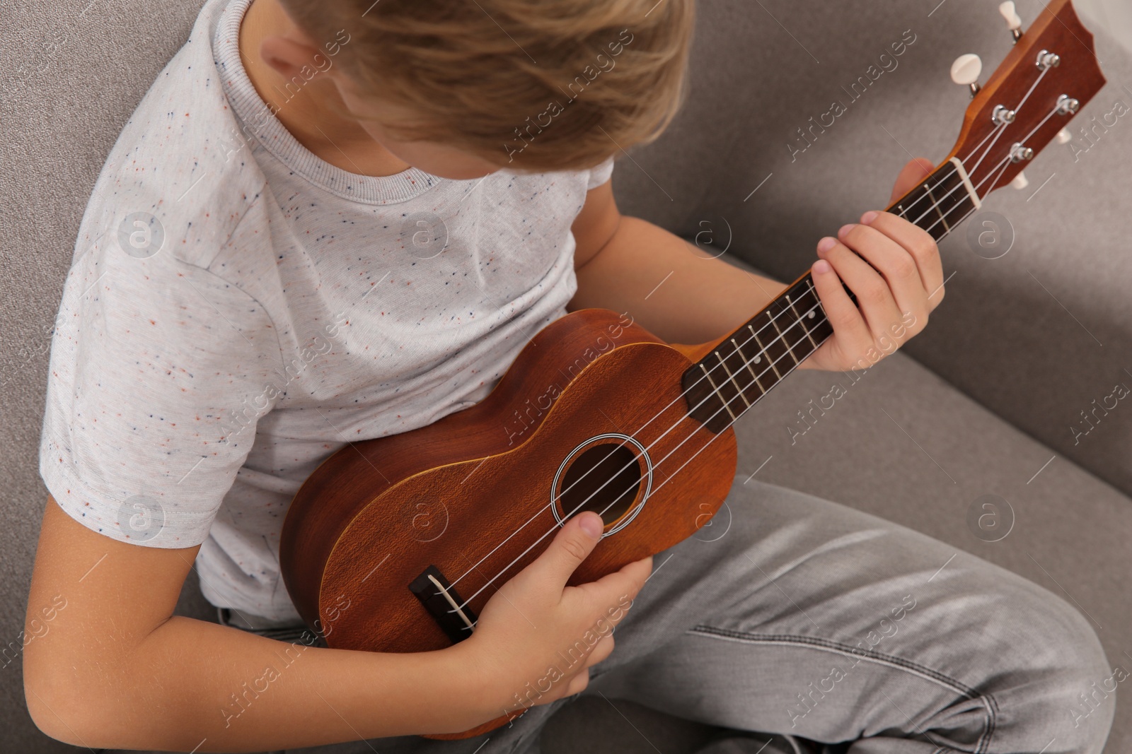 Photo of Little boy playing guitar on sofa in room, closeup