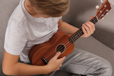 Photo of Little boy playing guitar on sofa in room, closeup