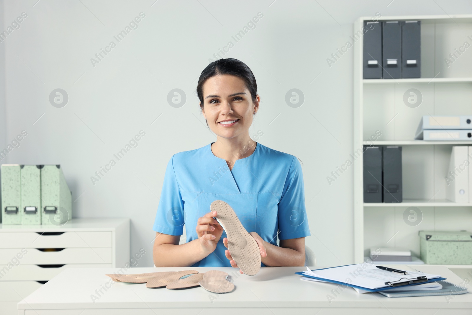 Photo of Beautiful female orthopedist showing insoles at table in hospital