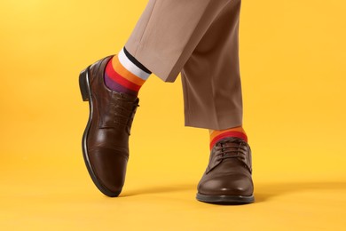 Photo of Man in stylish colorful socks, shoes and pants on yellow background, closeup