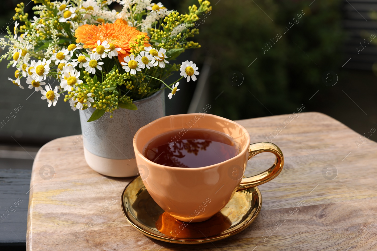 Photo of Cup of delicious chamomile tea and fresh flowers outdoors on sunny day