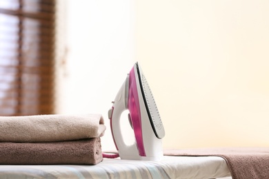 Photo of Modern iron and towels on board in room. Space for text