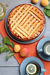 Photo of Tasty apricot pie and tea on grey wooden table, flat lay