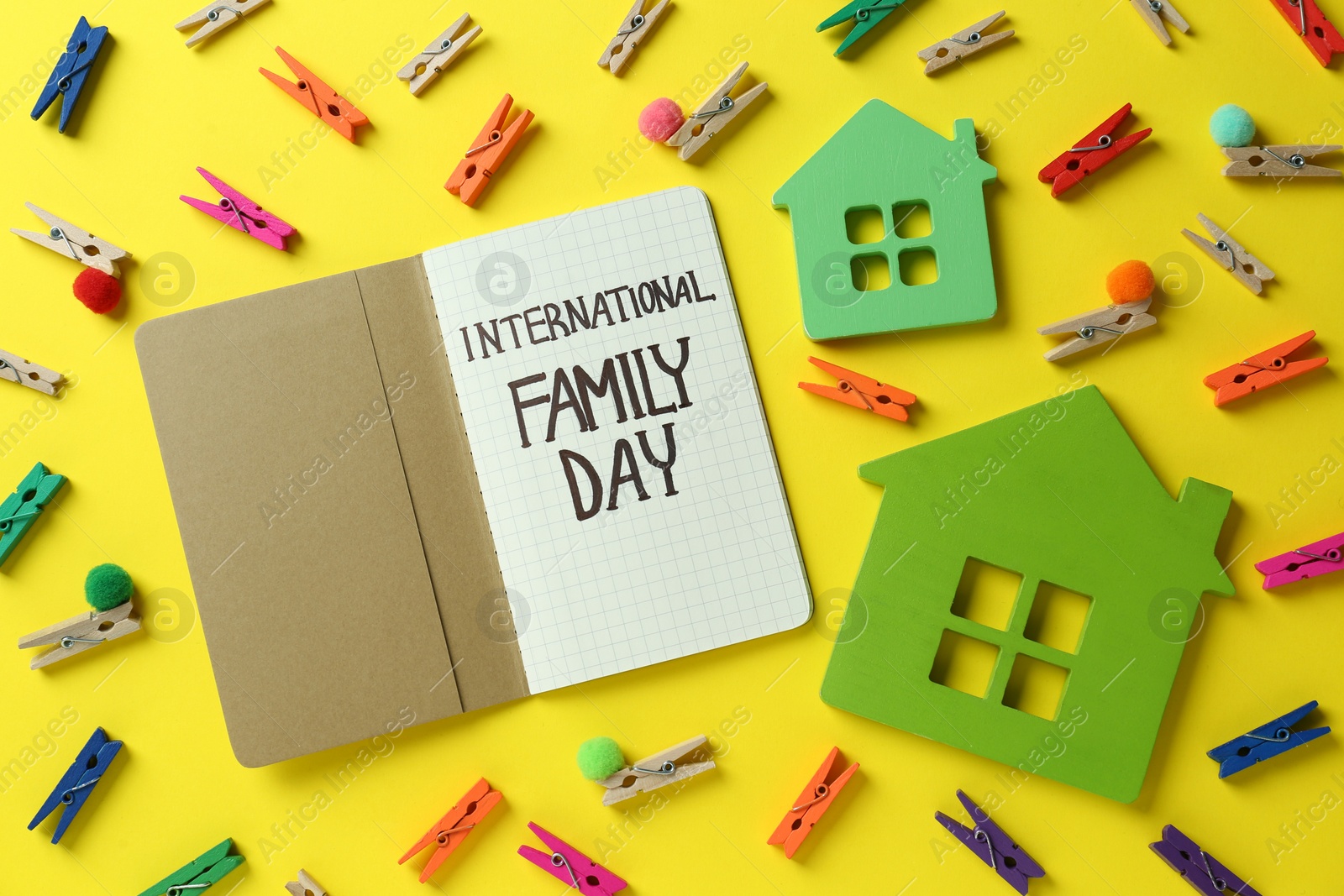 Photo of Happy International Family Day. Flat lay composition with notebook and house models on yellow background