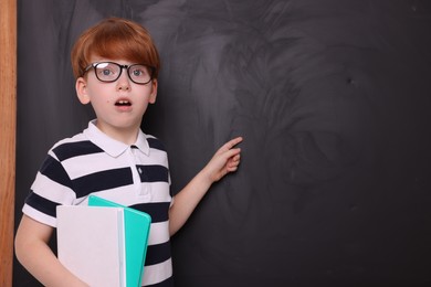 Photo of Shocked schoolboy in glasses with books pointing at something on blackboard. Space for text