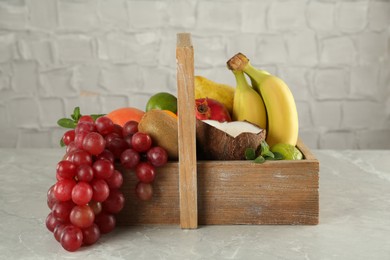 Wooden crate with different ripe fruits on grey table