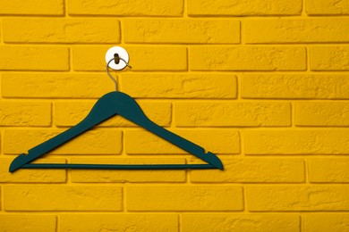 Photo of Empty clothes hanger on yellow brick wall, space for text