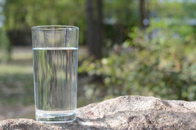 Photo of Glass of water on stone outdoors, space for text