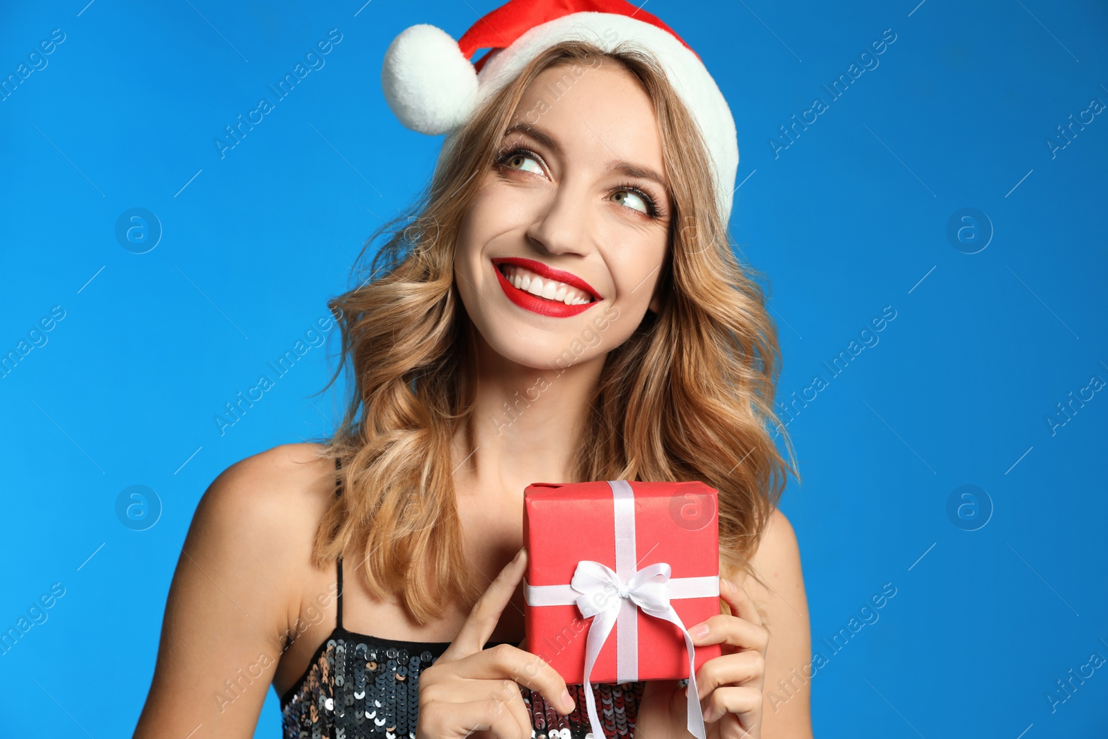 Photo of Happy young woman wearing Santa hat with Christmas gift on light blue background