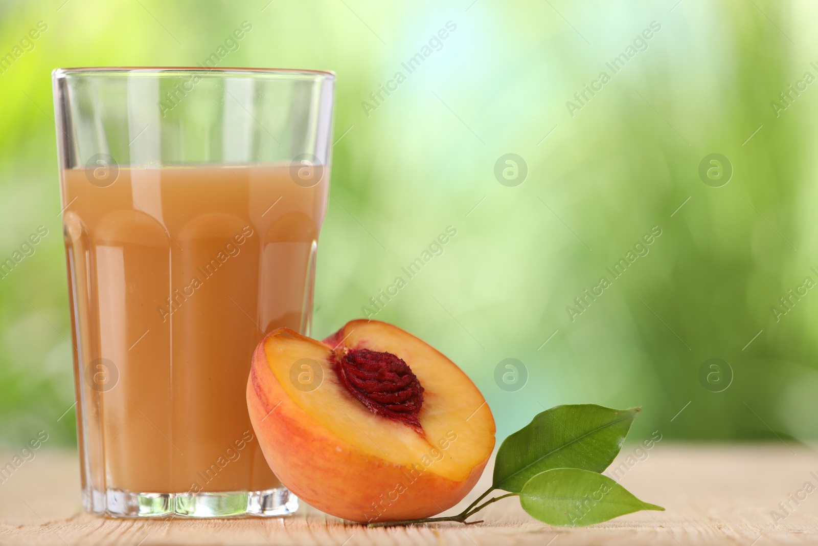 Photo of Tasty peach juice, fresh fruit and green leaves on wooden table outdoors, space for text