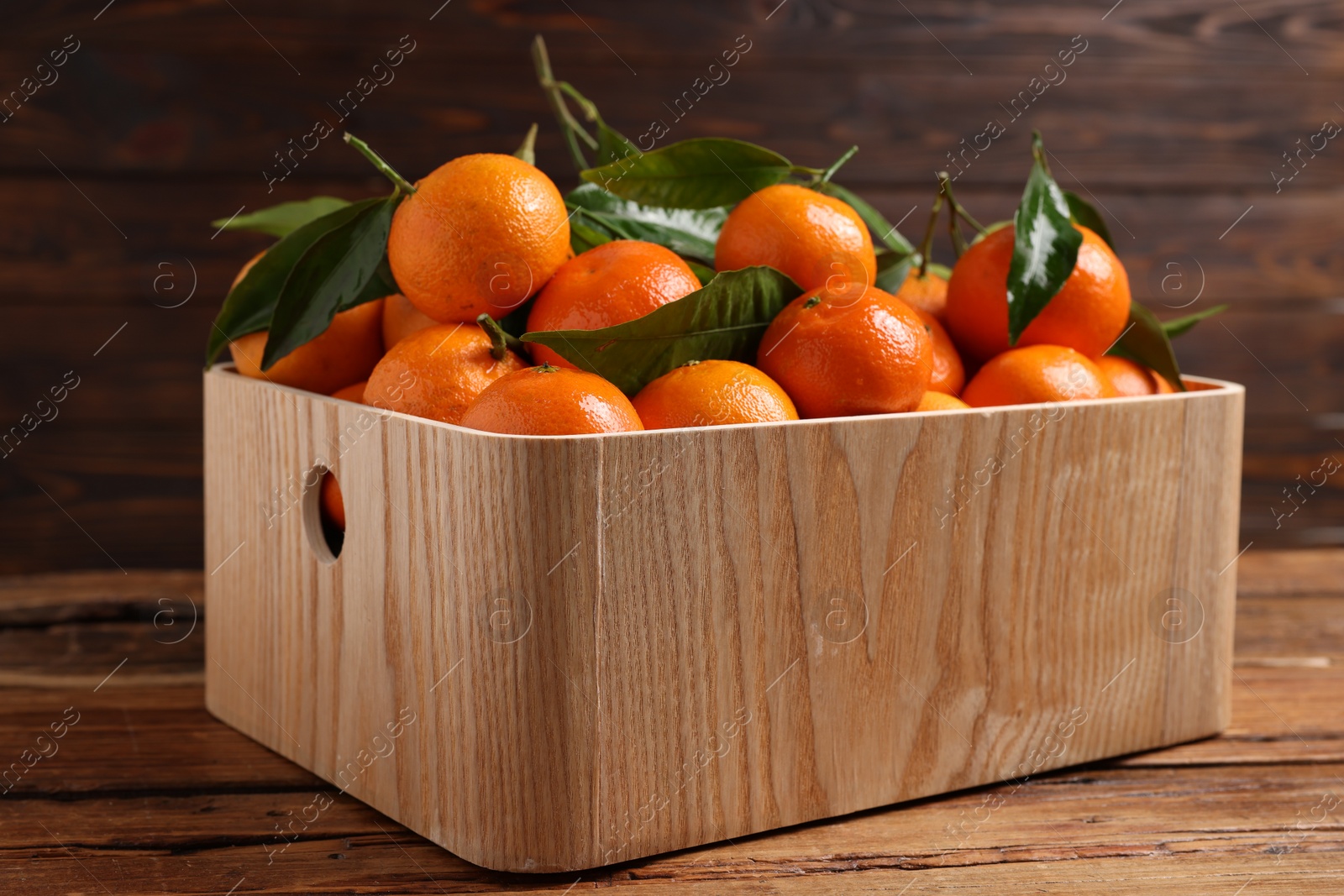 Photo of Fresh tangerines with green leaves in crate on wooden table