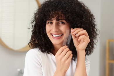 Photo of Young woman holding teeth whitening strips indoors