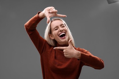 Photo of Casting call. Emotional woman showing frame gesture on grey background